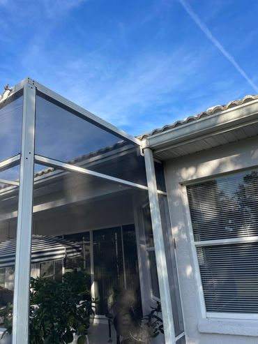 Screened patio enclosure attached to a house under a clear blue sky.