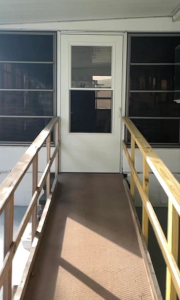 Ramp with wooden railings leading to a white door with glass panels.