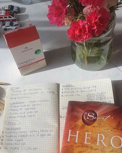 A diary, a book, Arbonne energy fizz sticks, a vase of flowers on a white table in the sun.