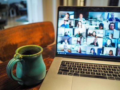 Mug and computer on a wooden desk showing a zoom call with lots of people from all over the world.