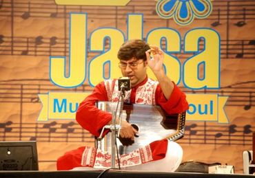 Musician performing traditional music on stage at Jalsa event.