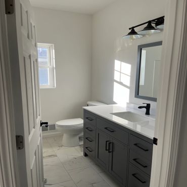 Modern bathroom with gray vanity, white countertop, and natural light.