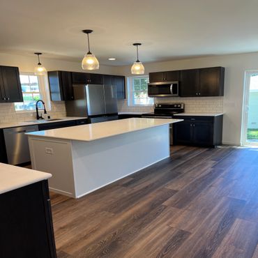 Modern kitchen with dark cabinets, white island, and stainless steel appliances.