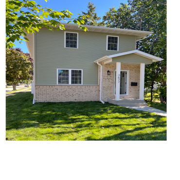 Two-story house with green siding and brick lower exterior under a clear blue sky.