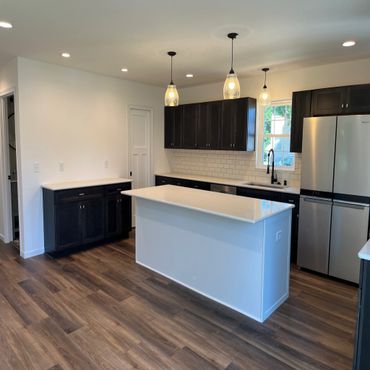 Modern kitchen with dark cabinets, white countertops, and wooden flooring.