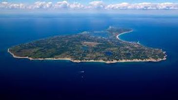 Aerial view of a lush green island surrounded by blue ocean under a partly cloudy sky.
