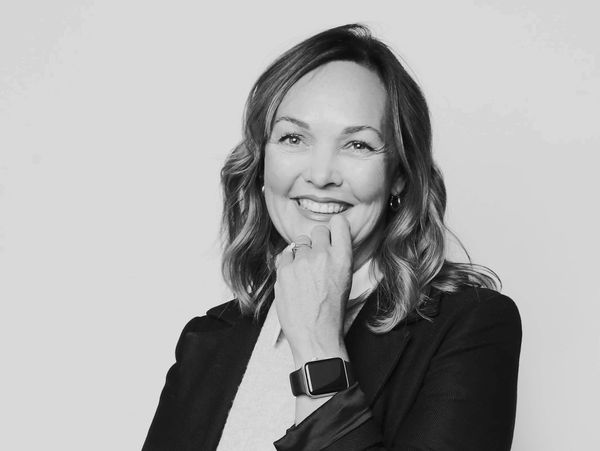 Smiling woman with wavy hair wearing a black blazer and smartwatch, posing confidently.