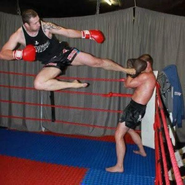 Martial artist delivering a flying kick in a ring.