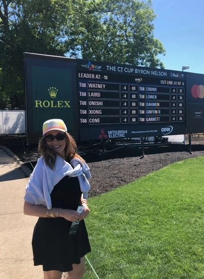Woman smiling in front of a golf leaderboard at The CJ Cup Byron Nelson.