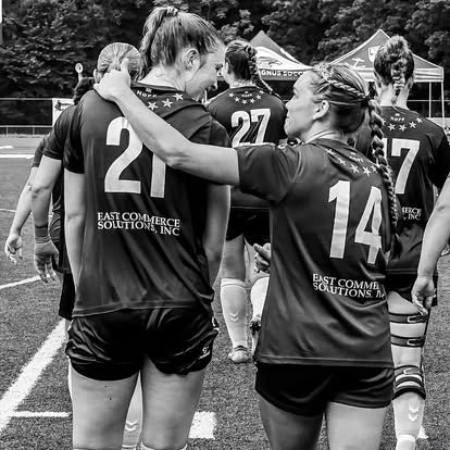 Two female soccer players share a supportive moment on the field.