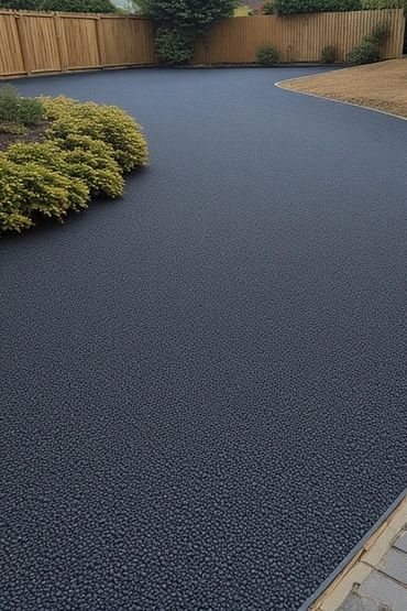 A smooth, dark rubber pebble driveway in a landscaped garden.