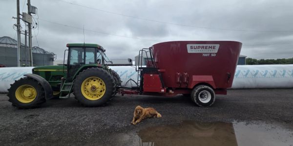 Tractor with feed mixer and a dog lying on wet ground.
