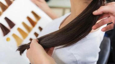 Hairdresser holding dark straight hair with color samples.