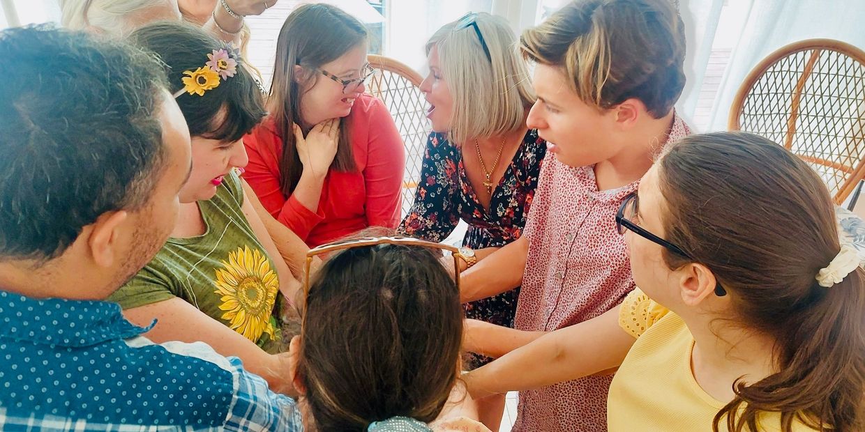 A diverse group of people joining hands in a circle indoors, sharing a moment of connection.