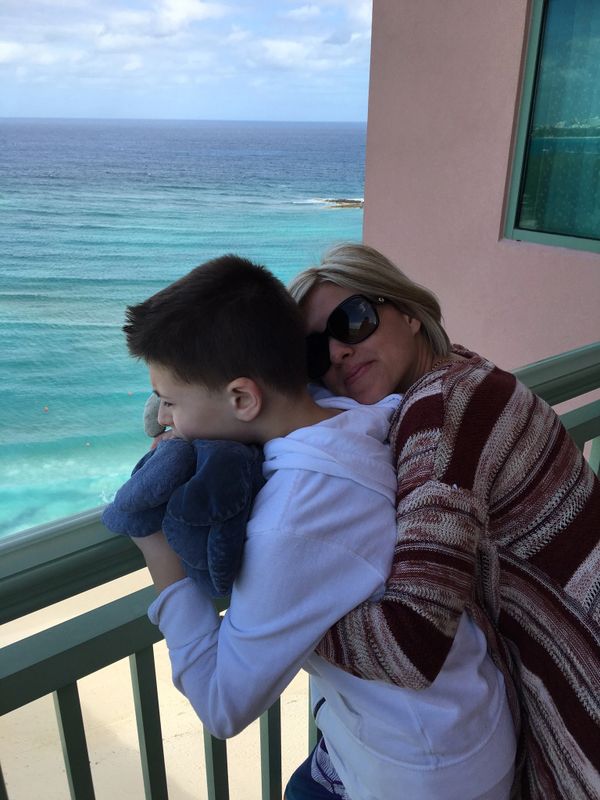 A woman hugs a boy on a balcony overlooking the ocean.