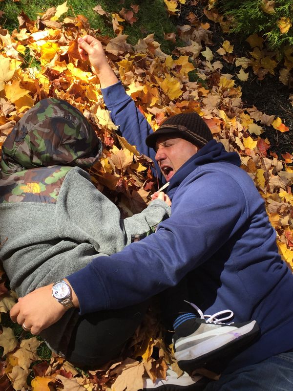 A man and child playing in autumn leaves on a sunny day.