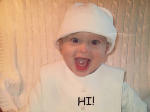 Happy baby wearing a white hat and bib with 'HI!' text.