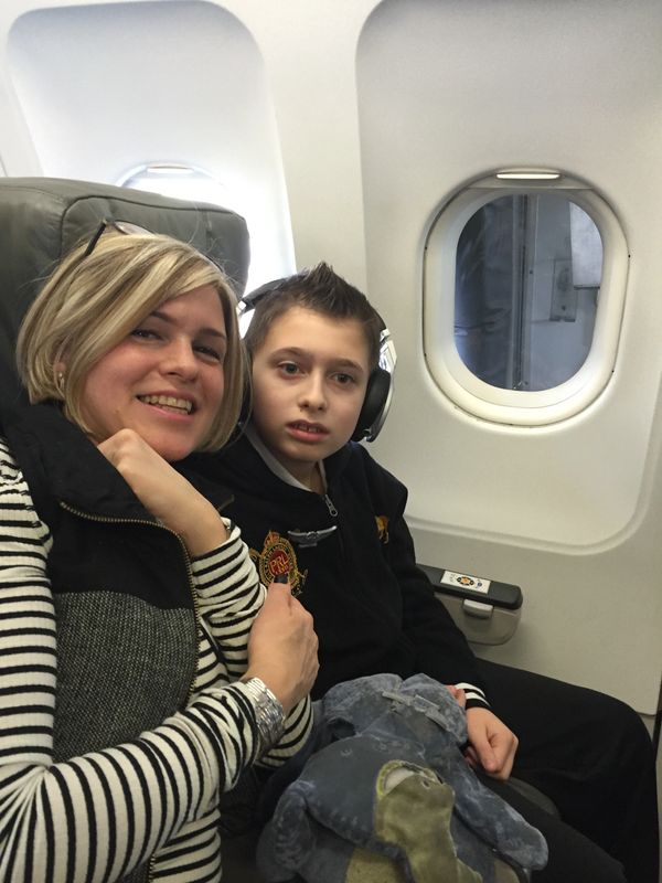 Mother and son seated together on an airplane, the boy wearing headphones.