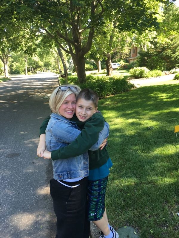 A woman and boy hugging on a sunny suburban street.