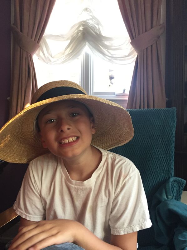 Smiling boy wearing a large straw hat indoors.