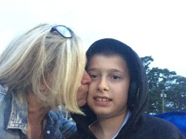 A woman kisses a boy on the cheek outdoors during dusk.