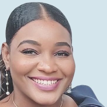 A close-up of a smiling woman with pearl earrings and neatly styled hair.