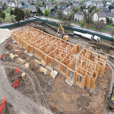 A wooden frame of a large building under construction in a suburban area.