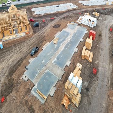 Aerial view of a residential construction site with concrete foundations and wooden framing.