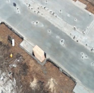 Aerial view of a construction site with a freshly poured concrete foundation slab.