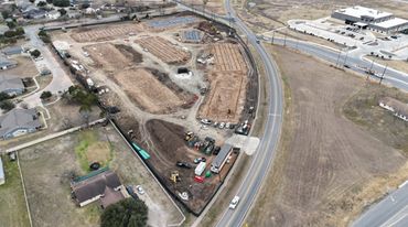 Aerial view of a construction site beside a curved road with equipment and nearby buildings.