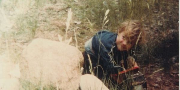 Child playing outdoors near rocks and grass.