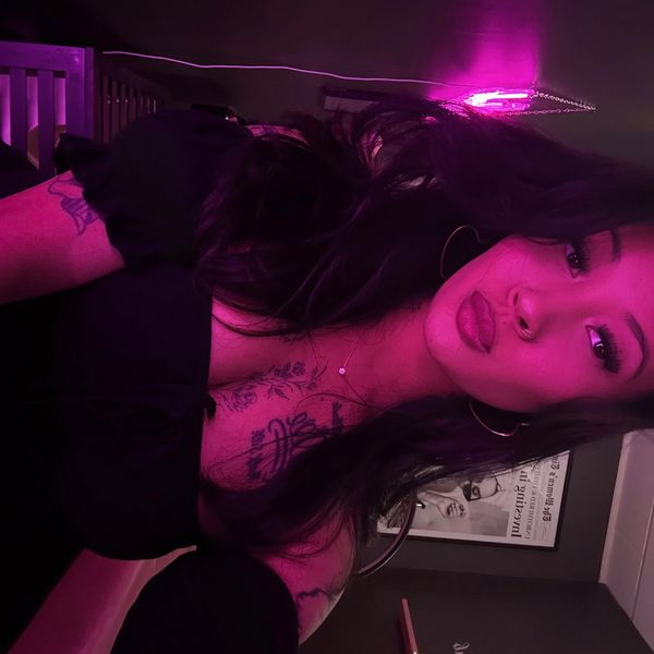 Young woman with tattoos and hoop earrings in pink neon light.