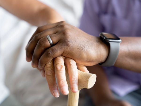 A younger person holds the hand of an older person gripping a walking cane.