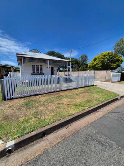 Small white house with a picket fence and clear blue sky.