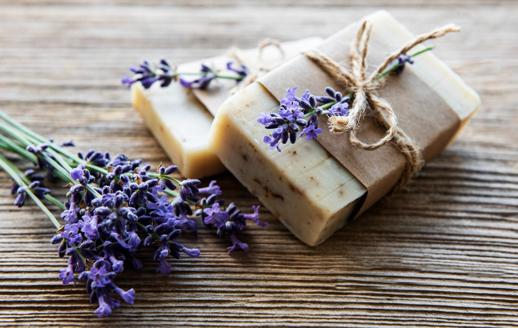 Two wrapped lavender soap bars with fresh lavender sprigs on a rustic wooden surface.