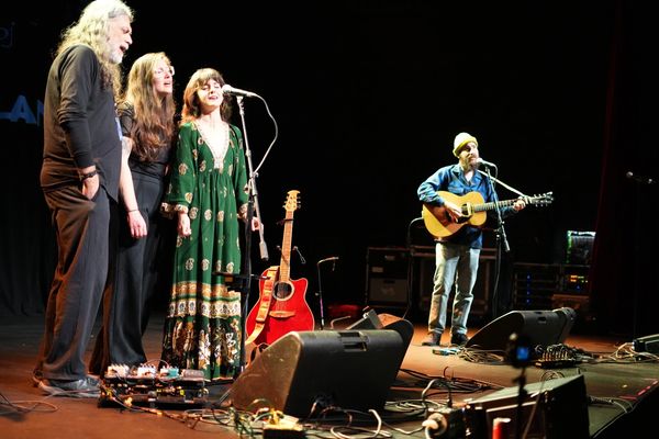 Four musicians performing on stage with guitars and microphones under stage lights.