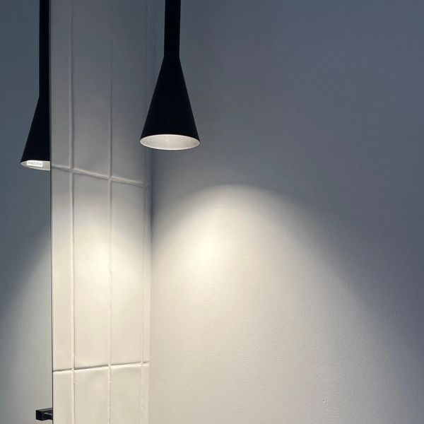 Minimalist black pendant lights illuminating a white tiled wall and plain white wall.
