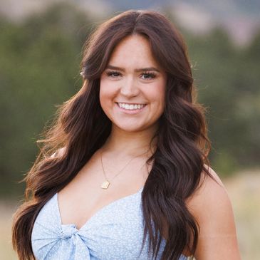 Young woman with long brown hair smiling outdoors in a light blue dress.