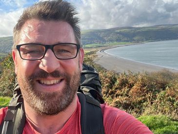 Man smiling with coastal landscape in the background.