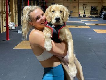 A woman joyfully holds a golden retriever puppy in a gym.