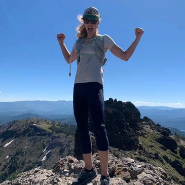 Angela on top of a mountain celebrating the summit view
