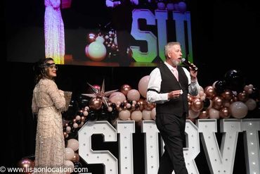 A man in a suit and a woman in a beaded dress on stage at a formal event.