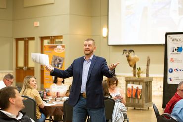 Man in blazer speaking to an audience in a conference room.