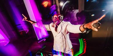 DJ in white suit energizes the crowd with vibrant lights and music.