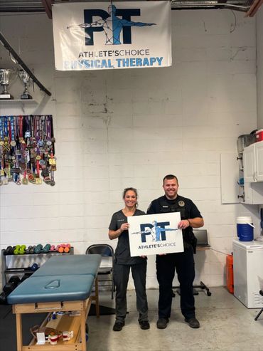 Two people holding a PT Athlete's Choice sign in a physical therapy clinic.