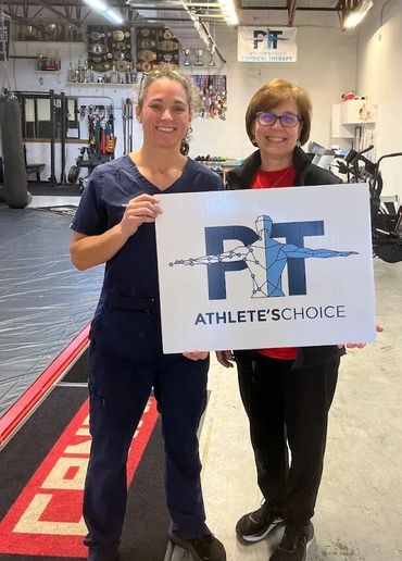 Two women holding a sign for PT Athlete's Choice in a gym setting.