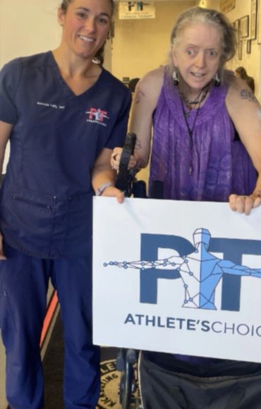 Two women holding a sign for PT Athlete's Choice in a therapy setting.