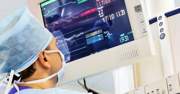 Surgeon monitors patient's vital signs on hospital screen during operation.