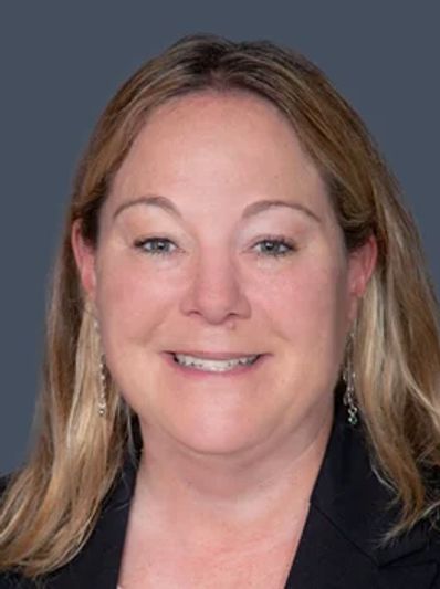 Smiling woman with blonde hair in front of a gray background.