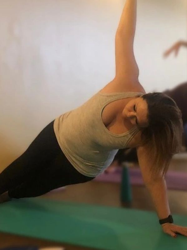 Woman doing a side plank yoga pose on a green mat indoors.